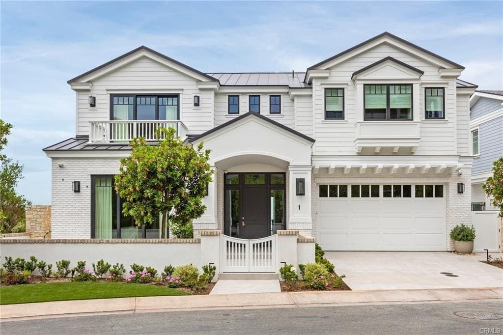 A white two-story coastal home in Dana Point seen from the street, with a covered entry, white garage doors, and clipped hedges.