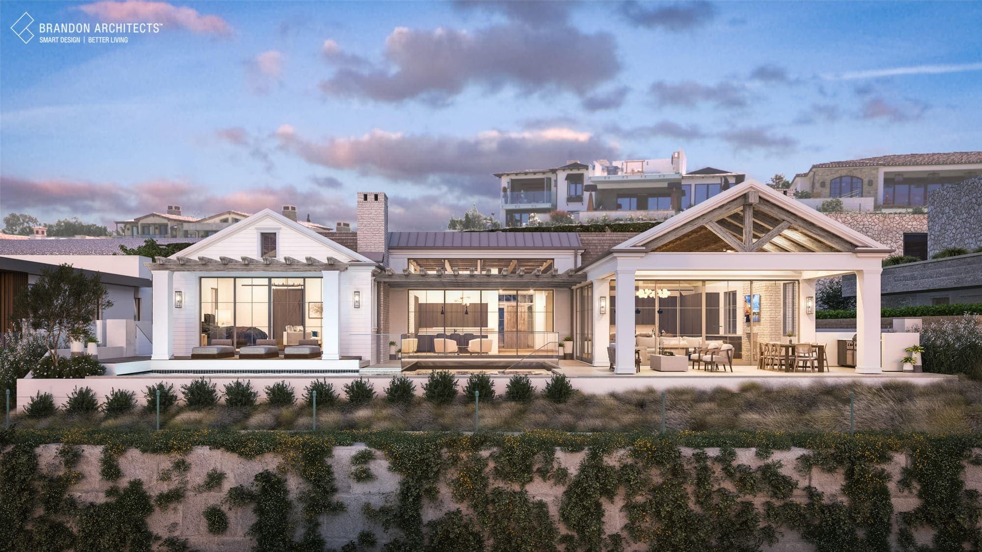 A white board-and-batten farmhouse in Dana Point at dusk with open-truss porches and warm interior light.