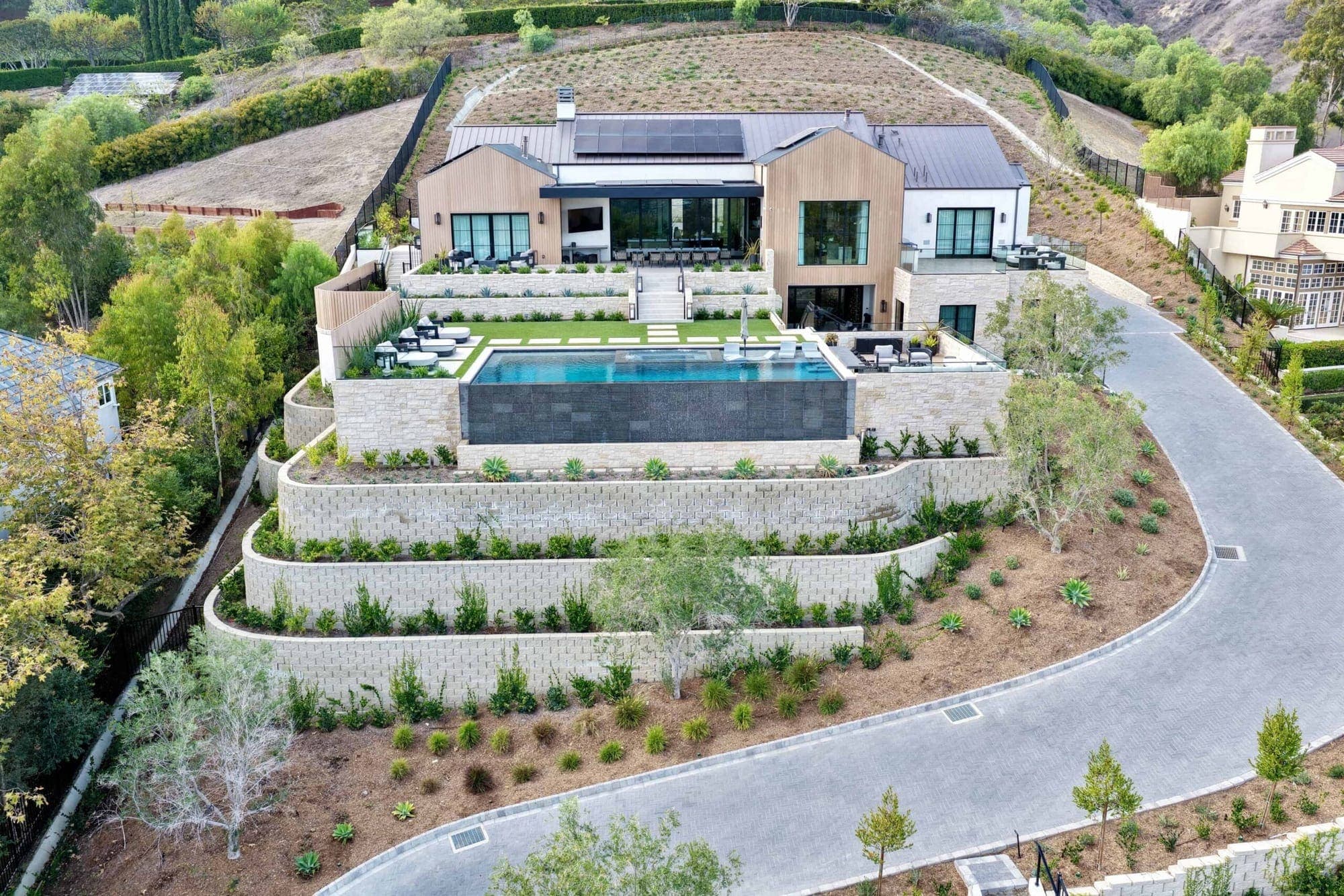 An aerial view of a hillside San Juan Capistrano home with terraced gardens and an infinity pool.