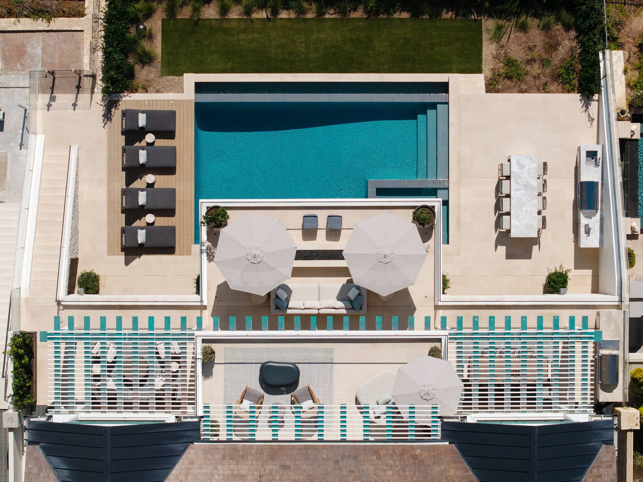 An infinity pool terrace seen from above, running along the edge of the bluff over the ocean.