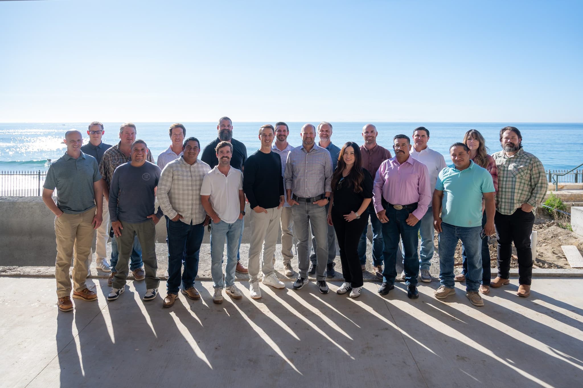 The Genova team, around twenty superintendents, project managers, designers and trade leads, standing together on a concrete terrace with the Pacific behind them.