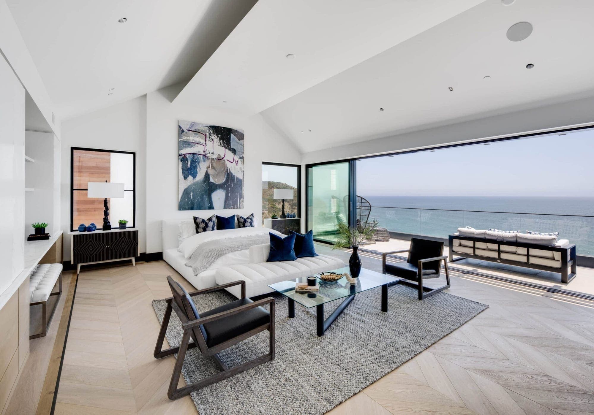 A living room with a wall of glass open to the ocean, filled with bright morning daylight.